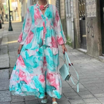 Vestido maxi floral em tons verdes e rosa usado por mulher com acessórios correspondente num cenário urbano.