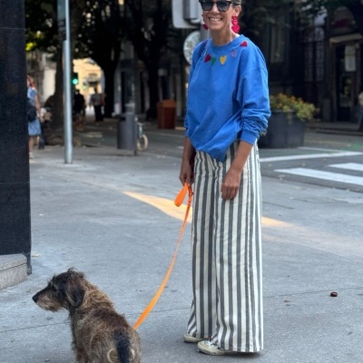 Mulher com sweat azul e calças às riscas a passear cão na rua