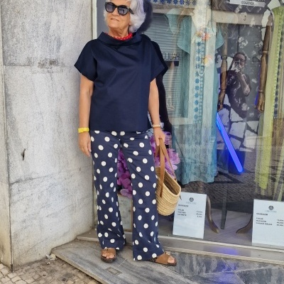 Mulher com roupa preta e azul às bolinhas junto a montra de loja