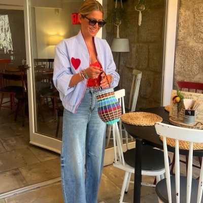 Mulher com blusa às riscas brancas e azuis com coração vermelho e mala de palha colorida