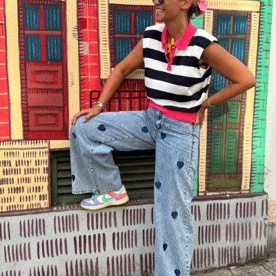 Mulher com calças de ganga com corações e camisola listrada junto a parede colorida com janelas pintadas