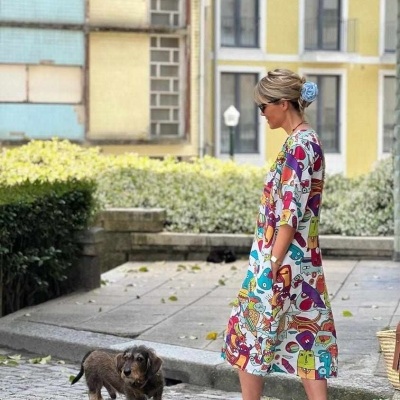 Mulher de vestido colorido com padrão animado e sapatos azuis junto a um cão numa rua urbana