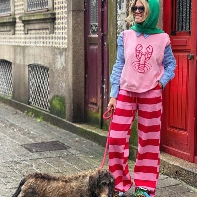 Pessoa com roupa colorida e cão de pelo longo numa rua com portas vermelhas.