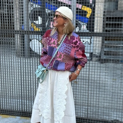 Mulher com casaco roxo e saia branca em frente a grelha metálica com grafite