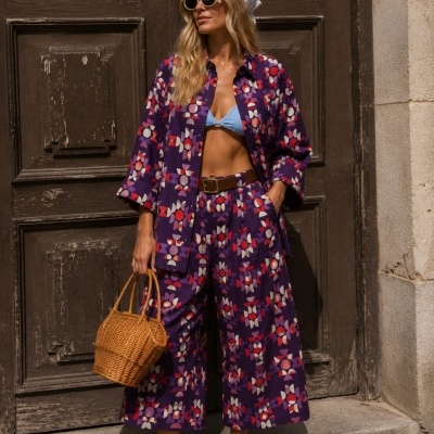 Conjunto feminino roxo com padrão geométrico, top azul, acessórios castanhos e sapatos bicolores.
