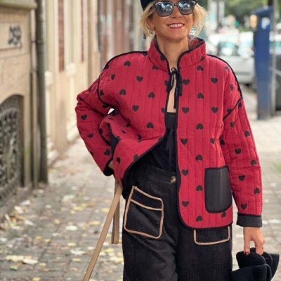 Mulher com casaco vermelho acolchoado com corações pretos e calças pretas com bolsos visíveis na rua