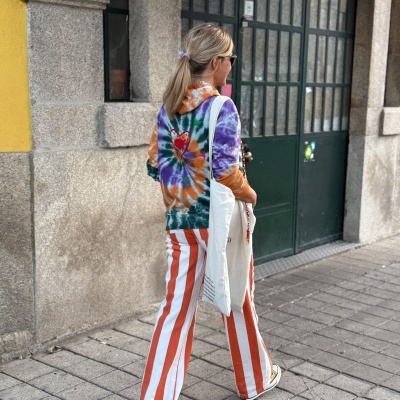 Mulher com camisola tie-dye e calças riscas largas caminhando numa rua