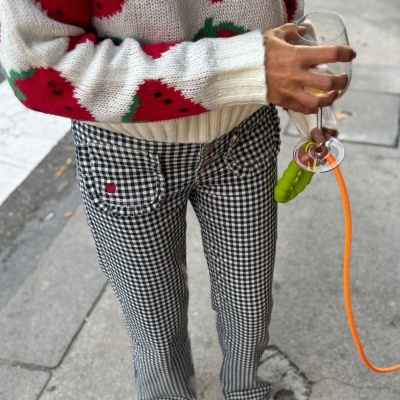 Pessoa com camisola bege com morangos e calças quadriculadas num passeio urbano segurando taça e coleira