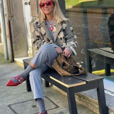 Mulher com casaco padrão animal cinzento e sapatos vermelhos sentada num banco preto ao ar livre