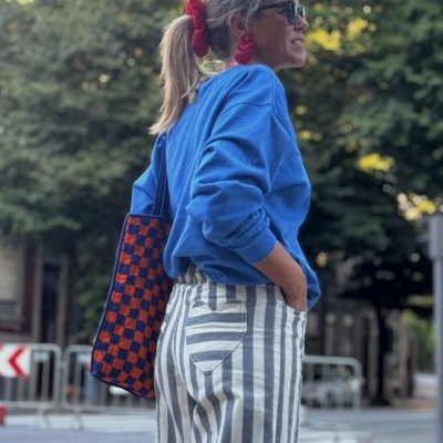 Mulher de perfil com sweatshirt azul, calças às riscas e bolsa xadrez em rua