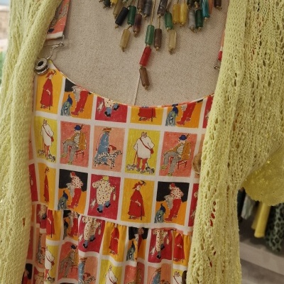 Vestido colorido com padrão de pessoas e cães, colete amarelo claro e colar colorido em manequim