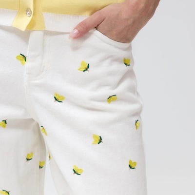 Calças brancas bordadas com padrão amarelo e verde junto com camisola amarela com botões e riscas