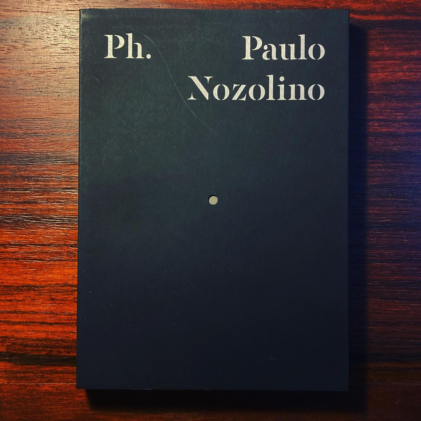 PH. 2 PAULO NOZOLINO ∙ SÉRGIO MAH ∙ RUI NUNES ∙ PAULO NOZOLINO Livro de capa preta com texto Paulo Nozolino sobre mesa de madeira escura
