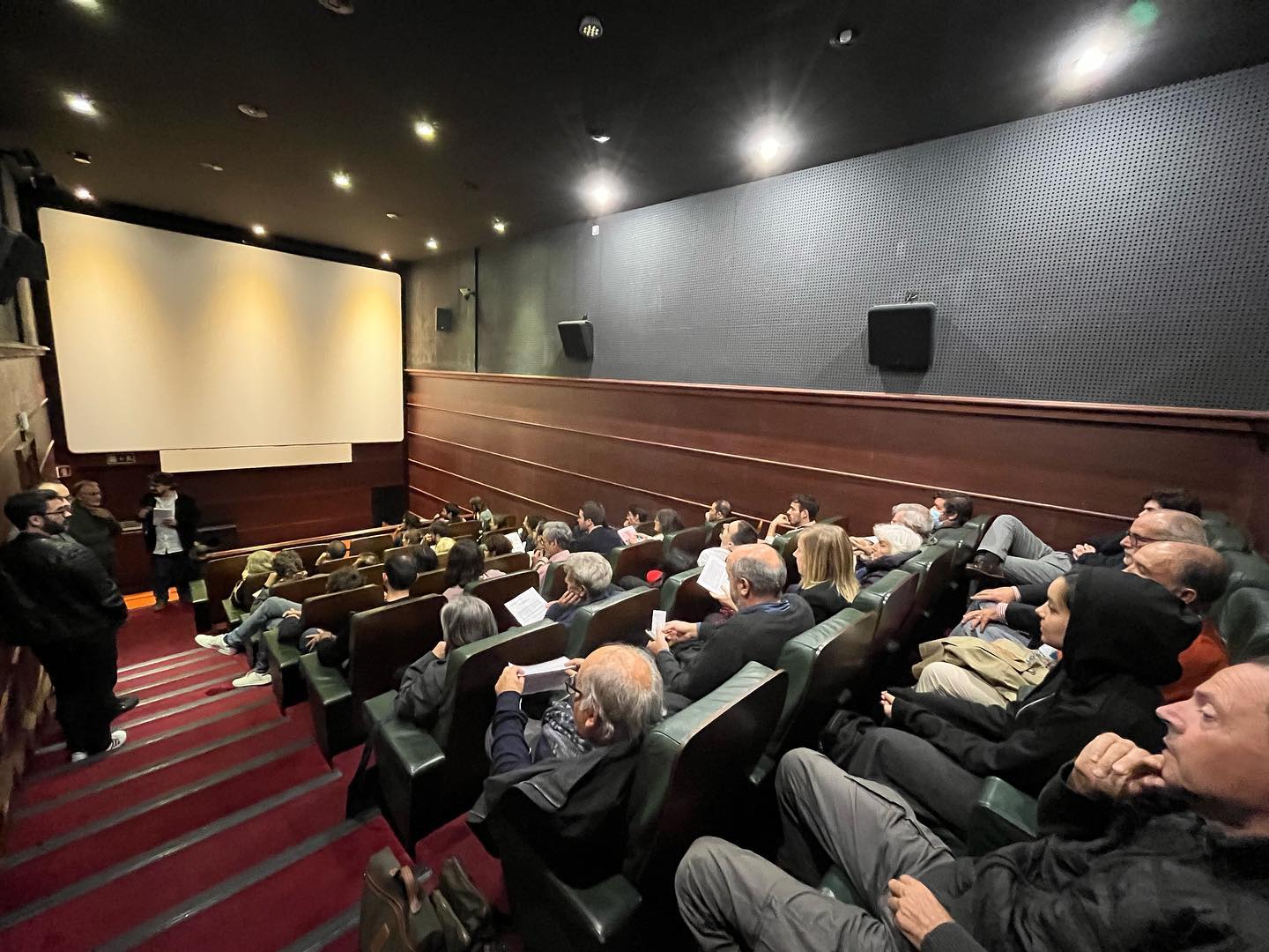 O CINEMA - UMA ESTÉTICA CRUA ∙ JOÃO PAULO DE OLIVEIRA CRUZ MENDES Sala de cinema com cadeiras pretas e pessoas a assistir a um filme