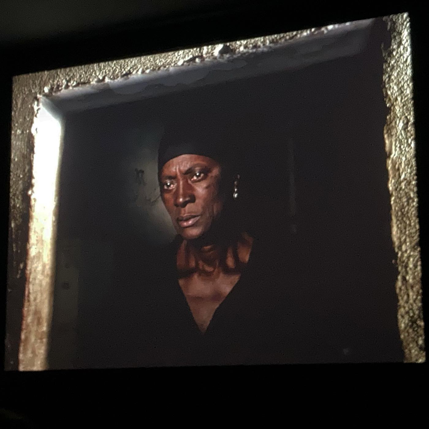 VITALINA VARELA • CADERNO DE RODAGEM • PEDRO COSTA Quadro com moldura dourada e retrato de pessoa com roupa preta e lenço na cabeça