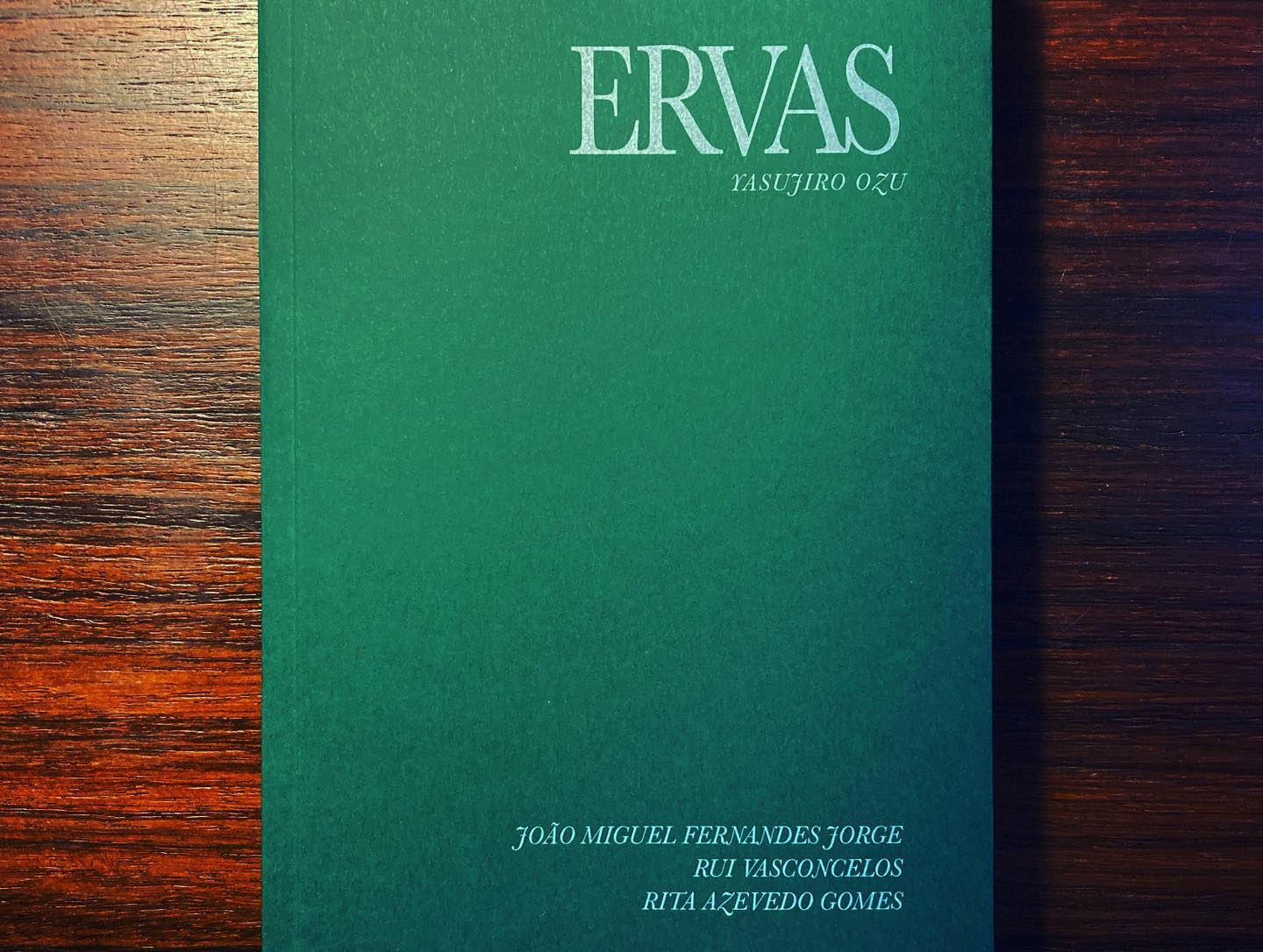 ERVAS ∙ YASUJIRO OZU ∙ JOÃO MIGUEL FERNANDES JORGE ∙ RUI VASCONCELOS ∙ RITA AZEVEDO GOMES Livro verde escuro com texto branco colocado sobre madeira escura