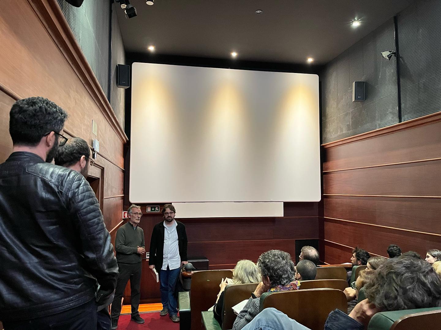 O CINEMA - UMA ESTÉTICA CRUA ∙ JOÃO PAULO DE OLIVEIRA CRUZ MENDES Auditório com pessoas sentadas, duas pessoas em pé e um grande ecrã branco na frente