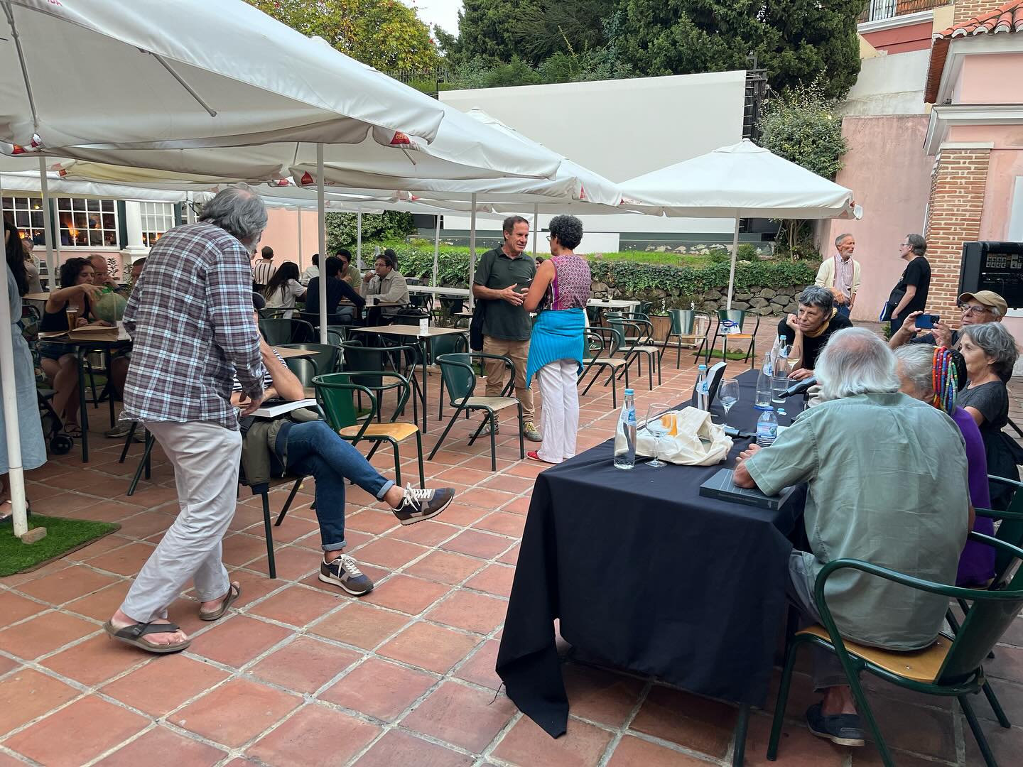 REGINA GUIMARÃES E SAGUENAIL ∙ DUAS PARALELAS QUE ÀS VEZES SE TOCAM OUTRAS VEZES NÃO ∙ INÊS SAPETA DIAS (ORG.) Área exterior com mesas, cadeiras, pessoas e guarda-sóis brancos em jardim