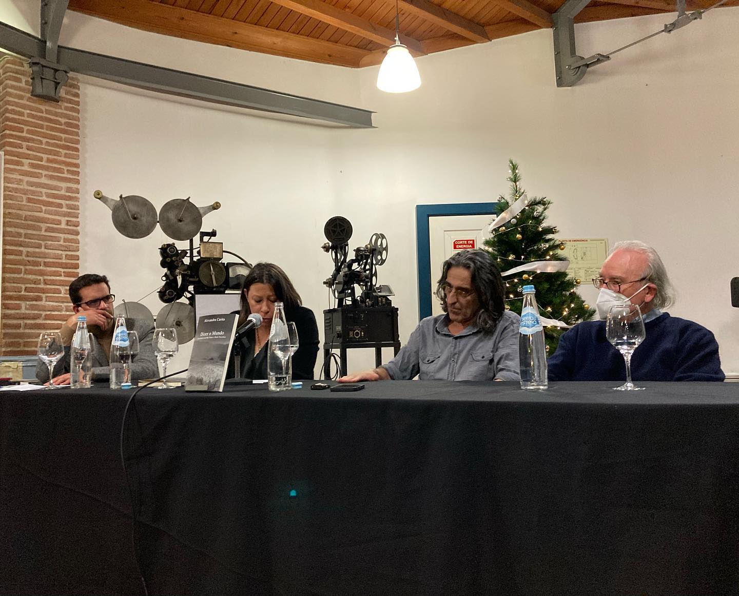 DIZER O MUNDO • CONVERSAS COM RUI NUNES E PAULO NOZOLINO • ALEXANDRA CARITA Mesa de conferência com quatro pessoas sentadas e decoração festiva