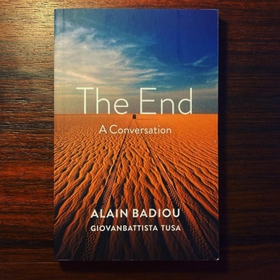 Livro 'The End A Conversation' com capa de deserto e céu azul sobre mesa de madeira escura