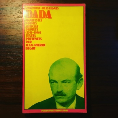 Caixa amarela e vermelha com fotografia de homem e texto DADA em vermelho
