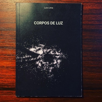 Livro capa preta com título CORPOS DE LUZ e autor Luís Lima sobre mesa de madeira