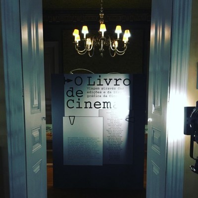 Painel de exposição com texto sobre cinema iluminado numa sala escura com candeeiro de teto