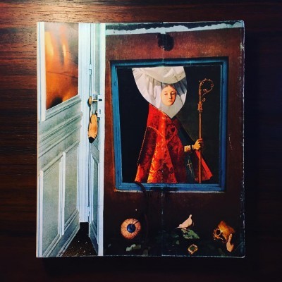 Livro com capa ilustrada de figura vestida de vermelho e chapéu branco sobre mesa de madeira