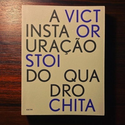 Livro com capa dura bege com texto preto e azul sobre uma mesa de madeira escura