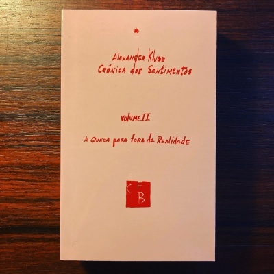 Livro branco com texto vermelho e logotipo numa superfície de madeira.