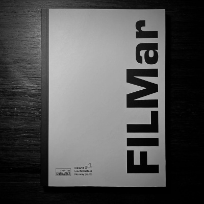 Livro ou revista capa branca com texto FILMar em preto sobre mesa de madeira escura