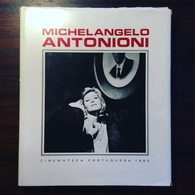 Livro Michelangelo Antonioni com capa branca, texto vermelho e imagem preta e branca