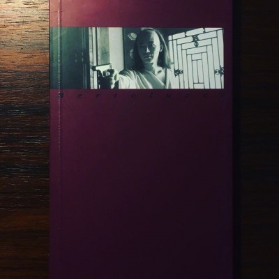 Capa de livro com imagem a preto e branco de mulher apontando arma e fundo de janela de grades