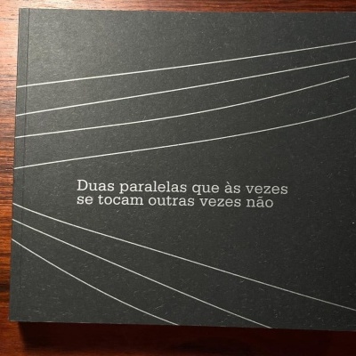 Livro ou caixa preta com linhas brancas paralelas e texto na capa sobre mesa de madeira