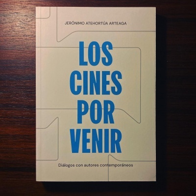 Capa de livro branco com título 'LOS CINES POR VENIR' em azul e texto adicional em preto sobre superfície de madeira