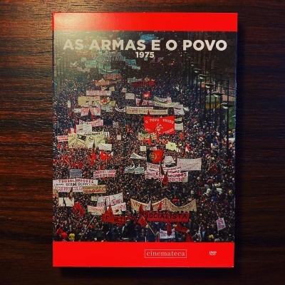 Capa de DVD vermelho com imagem de manifestação e texto AS ARMAS E O POVO 1975
