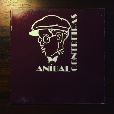 Capa de álbum castanho escuro com ilustração branca de homem com boné e texto ANÍBAL CONTREIRAS