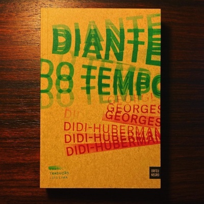 Capa de livro castanho com textos em verde e vermelho sobre fundo de madeira escura