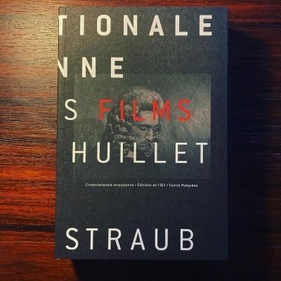 Livro com capa preta com texto branco e vermelho sobre superfície de madeira escura