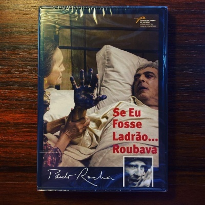 Capa de DVD azul com imagem de homem deitado e mulher segurando sua mão e texto vermelho.