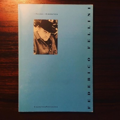 Capa de livro azul com título FEDERICO FELLINI e fotografia em preto e branco de um homem de chapéu.