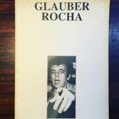Capa de livro branco com título Glauber Rocha e foto preto e branco de homem apontando.