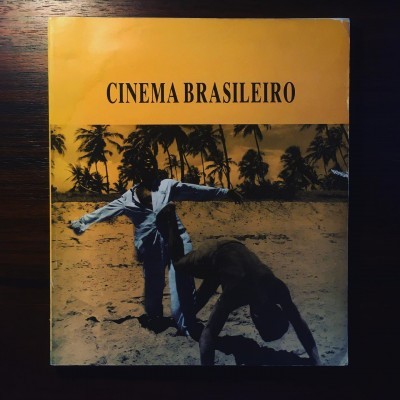 Capa de livro amarelo com foto de duas pessoas na praia e texto 'CINEMA BRASILEIRO'