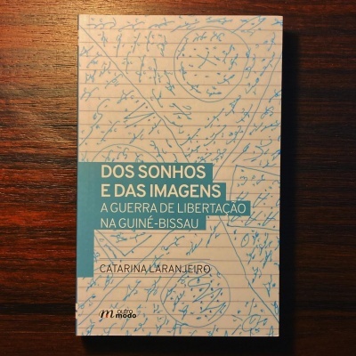 Livro sobre a guerra de libertação na Guiné-Bissau com capa em bege e azul sobre mesa de madeira