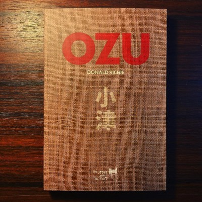 Livro OZU de capa castanha texturizada com título vermelho sobre mesa de madeira