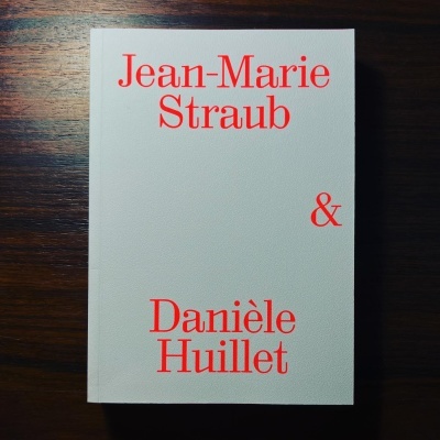 Livro com capa branca e texto vermelho com nomes dos autores sobre madeira escura