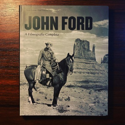 Capa do livro John Ford com homem montado num cavalo em cenário desértico a preto e branco