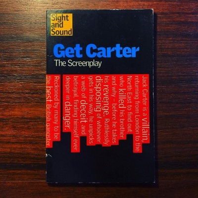 Capa de livro preta com texto azul, branco e vermelho, sobre mesa de madeira escura