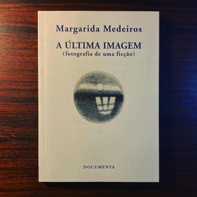 Livro 'A ÚLTIMA IMAGEM' de Margarida Medeiros em capa branca sobre mesa de madeira escura