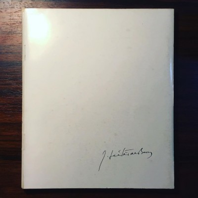 Livro branco com assinatura preta no canto sobre mesa de madeira